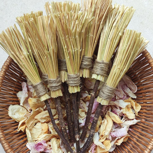 Balais de sorcière artisanal à grignoter en lin et noisetier, posés sur des pétales séchés dans une corbeille.